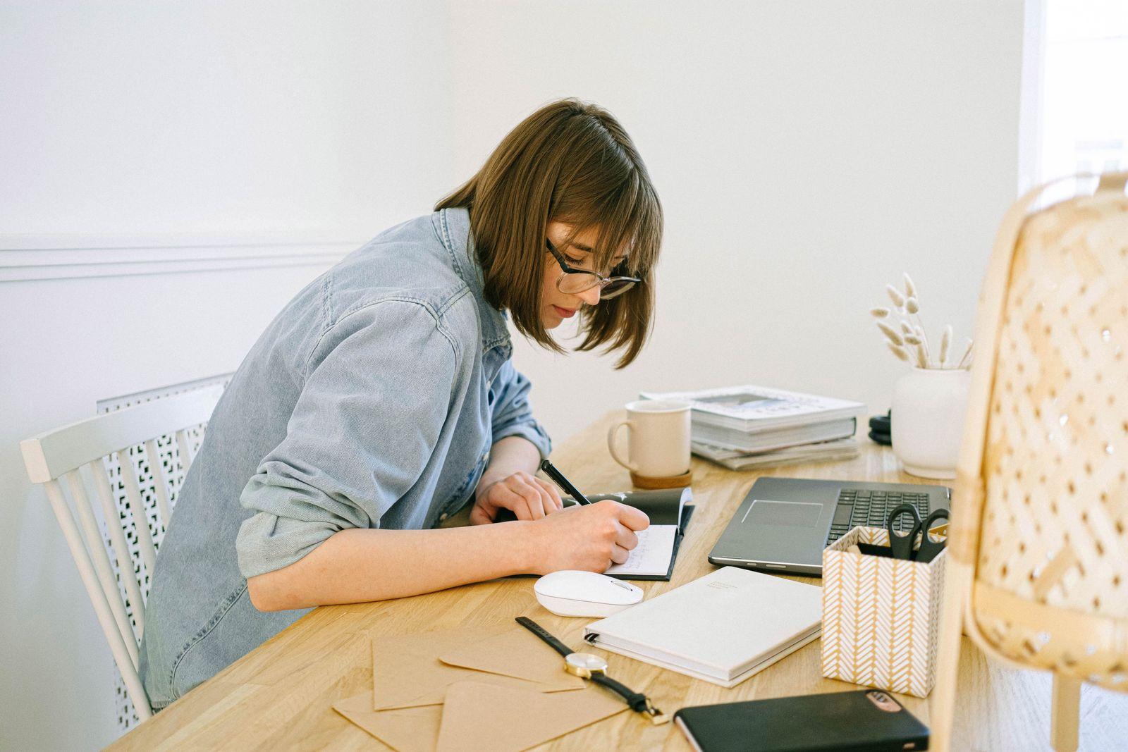 A person writing notes and planning a single task at a desk with a laptop